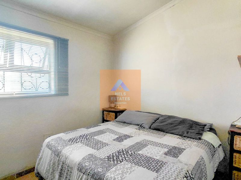 A functional bedroom featuring a window with security bars and built-in wall shelving.