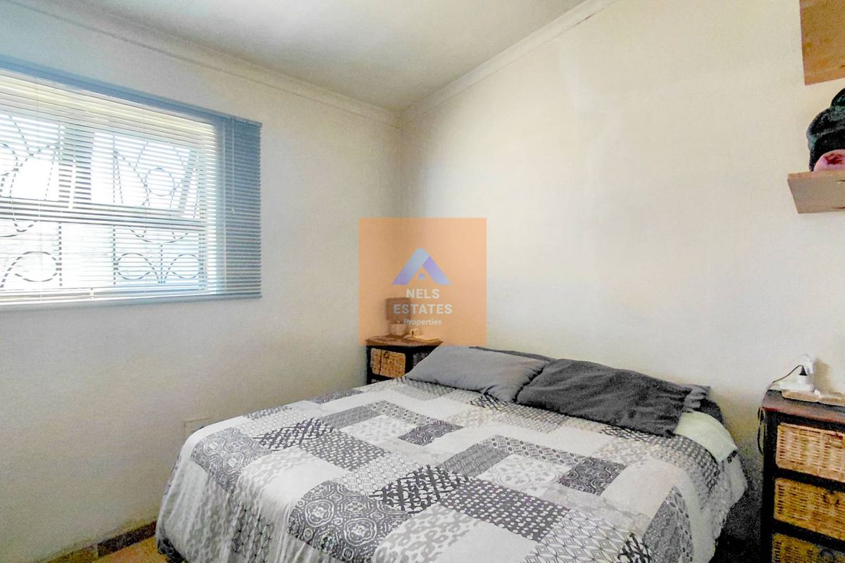 A functional bedroom featuring a window with security bars and built-in wall shelving.