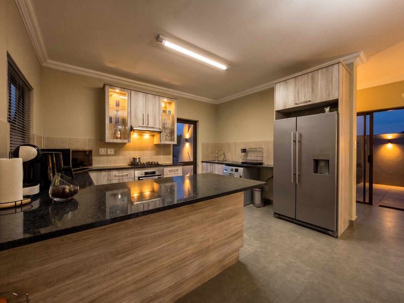 Modern kitchen featuring granite countertops, wood-finish cabinetry, built-in appliances, and tiled flooring with direct access to an outdoor patio area.
