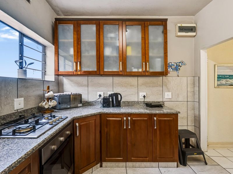 Functional kitchen featuring wooden cabinetry, granite countertops, a gas hob, and built-in oven with tiled backsplash and flooring.