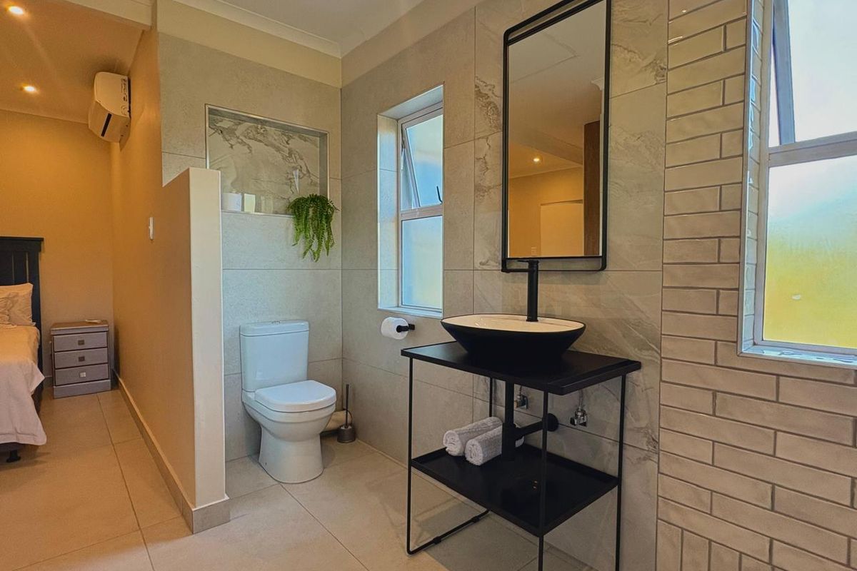 Modern bathroom featuring a sleek vessel sink, black metal vanity, tiled finishes, and a private toilet area with a recessed niche.