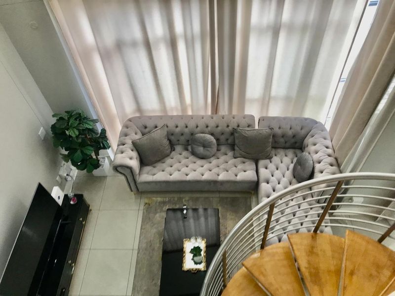 A high-angle view of a modern living room featuring tiled floors, large windows with floor-to-ceiling curtains, and a spiral staircase.