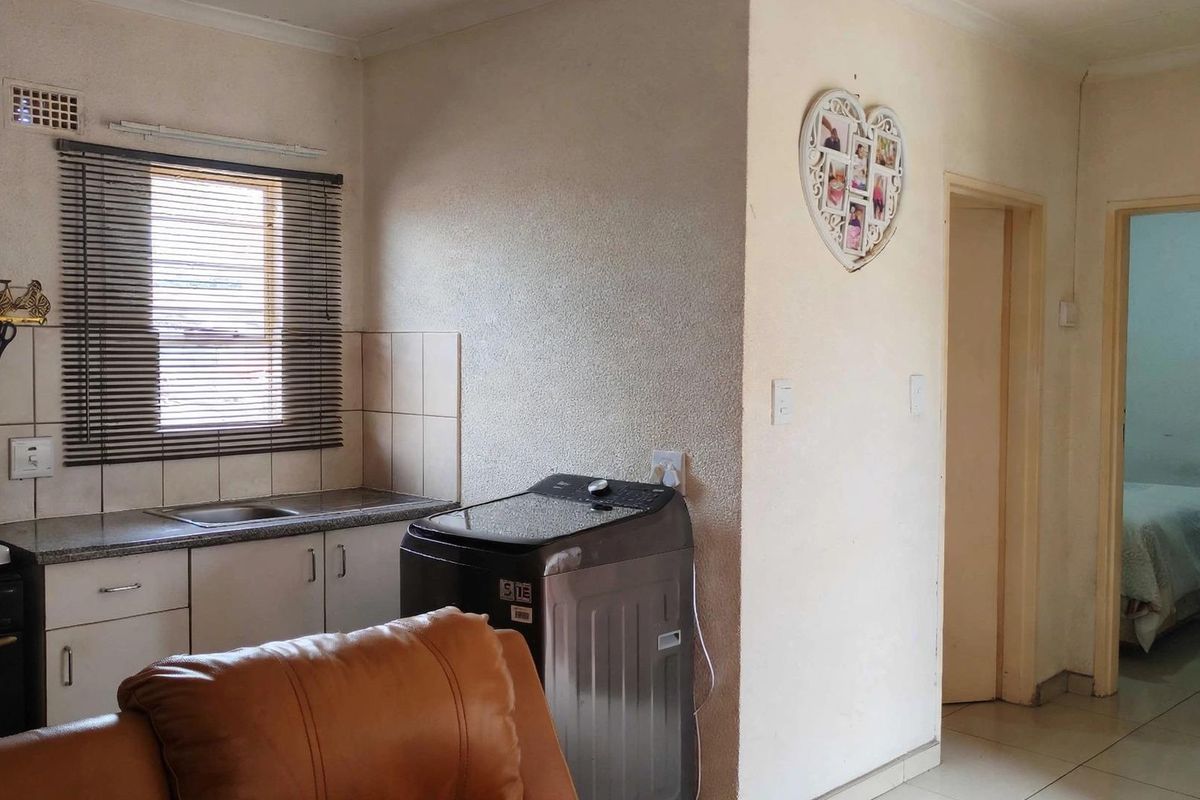 A functional kitchen area featuring built-in cabinetry, a stainless steel sink, tiled splashbacks, and an integrated oven, with adjacent access to other rooms.