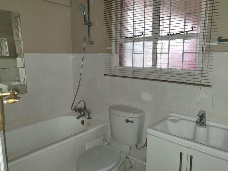 A functional bathroom featuring a bathtub with shower attachment, a standard toilet, and a vanity basin, requiring cosmetic updates to improve its overall condition.