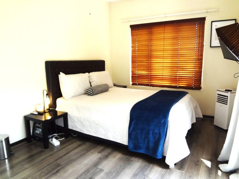 A well-lit bedroom featuring modern laminate flooring and fitted wooden venetian blinds, providing a comfortable and neutral living space.