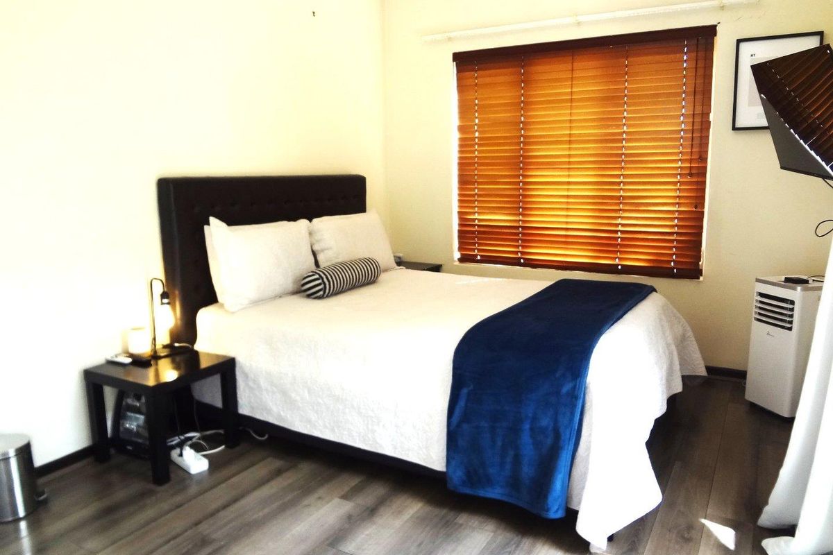 A well-lit bedroom featuring modern laminate flooring and fitted wooden venetian blinds, providing a comfortable and neutral living space.