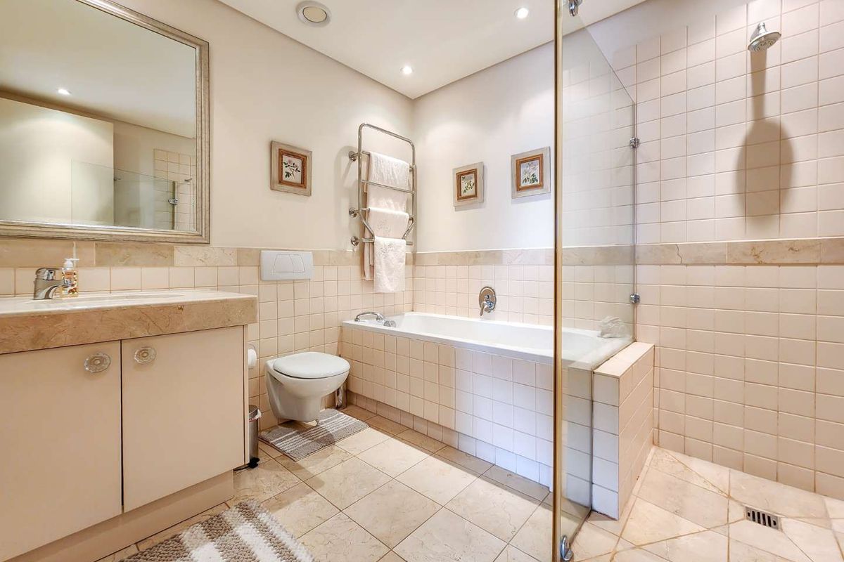 A well-maintained bathroom featuring a stone-topped vanity, wall-mounted toilet, bathtub, and a separate glass-enclosed shower area with neutral tiling.