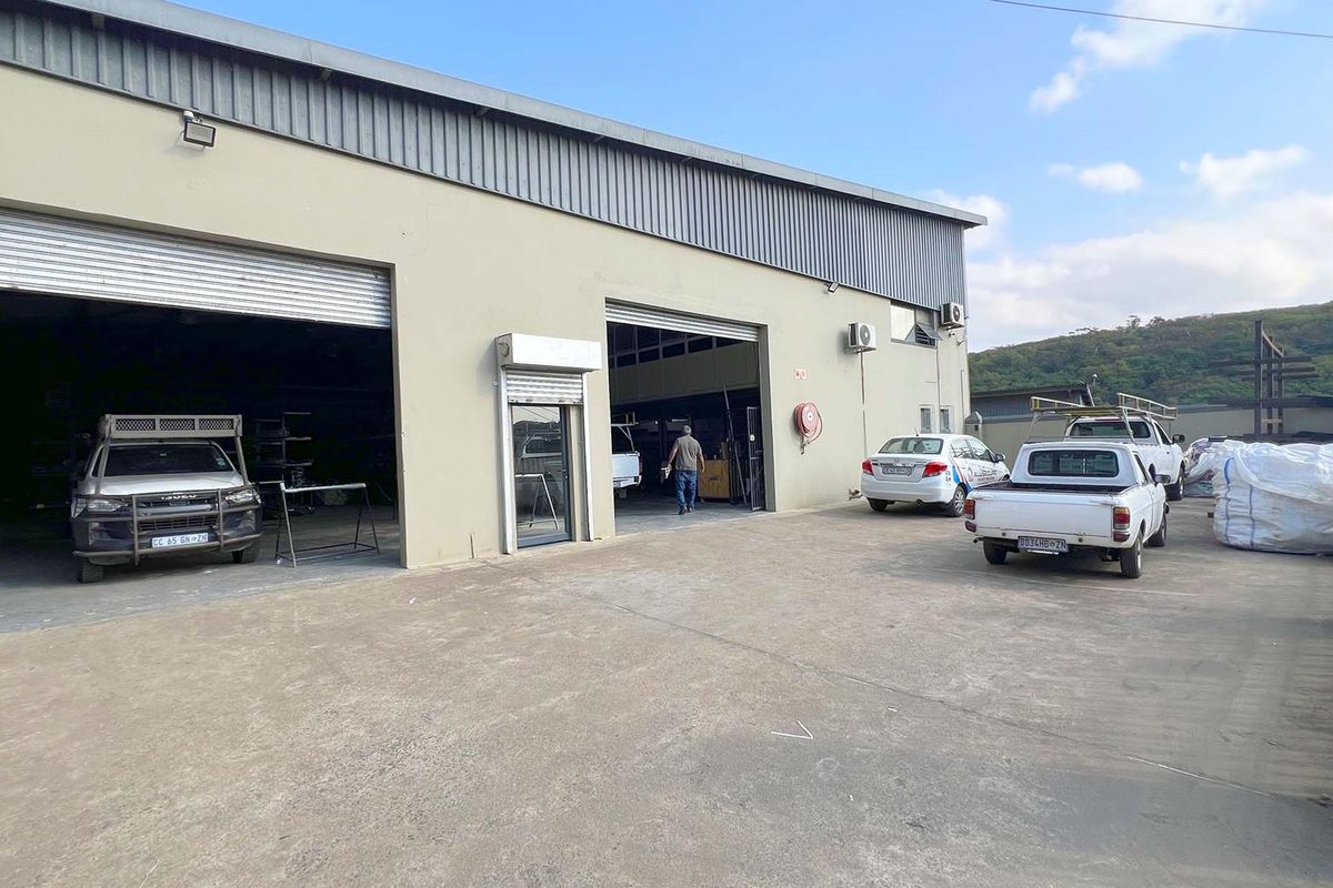 Industrial warehouse facility featuring large roller shutter access doors, concrete yard space, and perimeter security fencing.