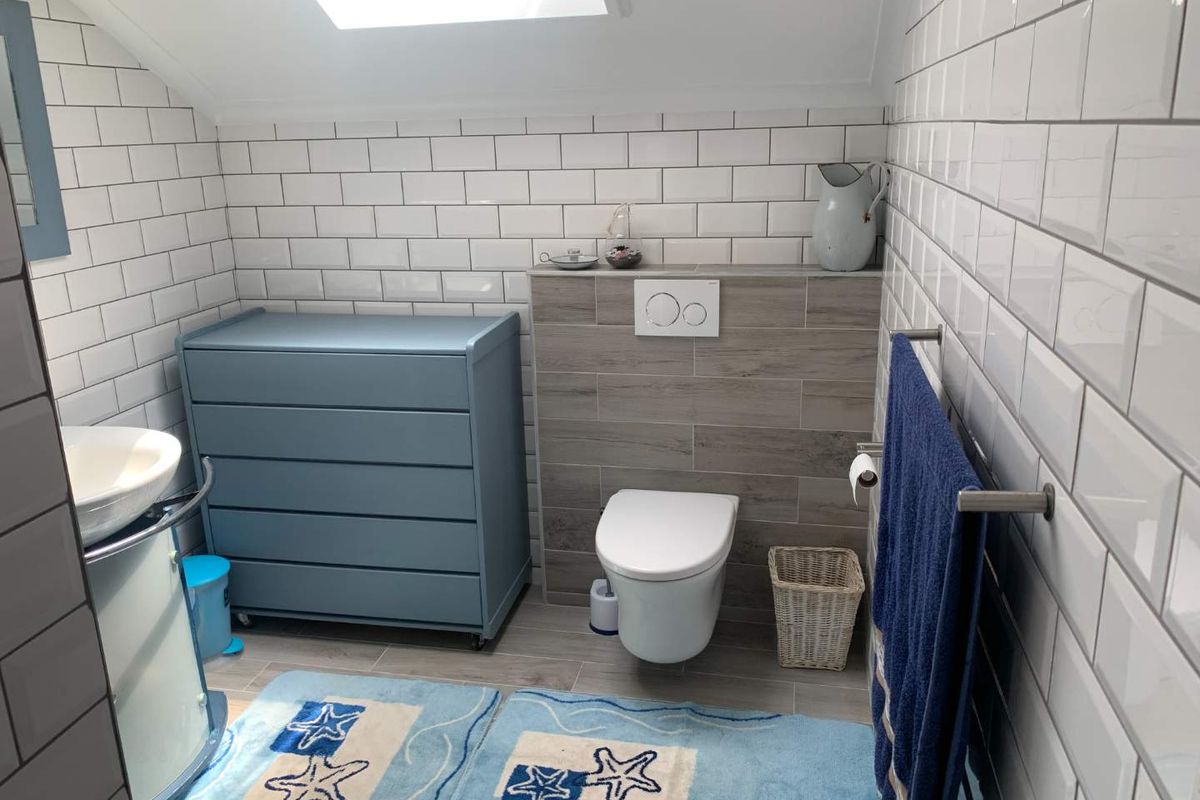 A modern bathroom featuring white subway wall tiles, a wall-mounted toilet with a concealed cistern, and a skylight providing natural light.