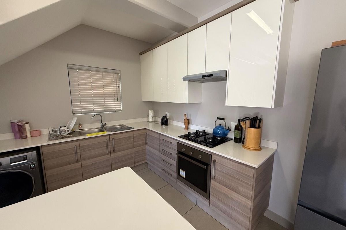 Modern kitchen featuring wood-grain lower cabinetry, white high-gloss upper cabinets, stone countertops, built-in oven, gas hob, and integrated extractor fan.