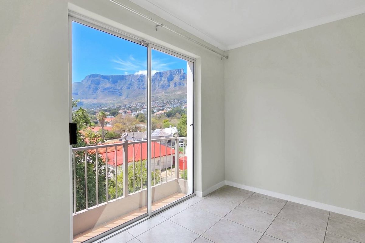 An empty bedroom featuring tiled flooring and a sliding glass door that opens onto a balcony with scenic mountain views.
