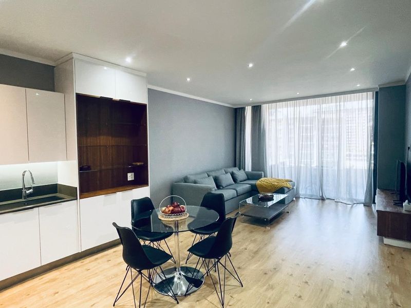 Modern open-plan living area featuring sleek kitchen cabinetry, recessed lighting, and light laminate flooring, creating a bright and cohesive living space.