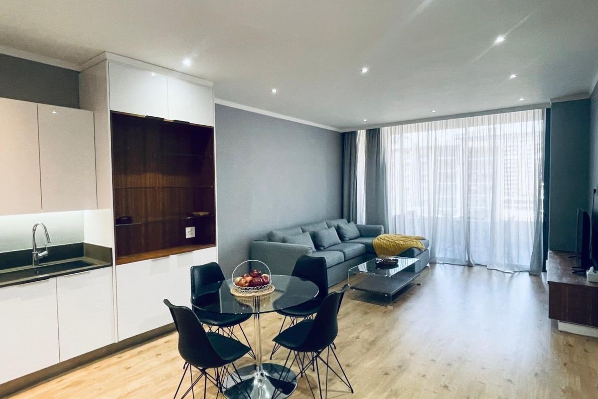 Modern open-plan living area featuring sleek kitchen cabinetry, recessed lighting, and light laminate flooring, creating a bright and cohesive living space.