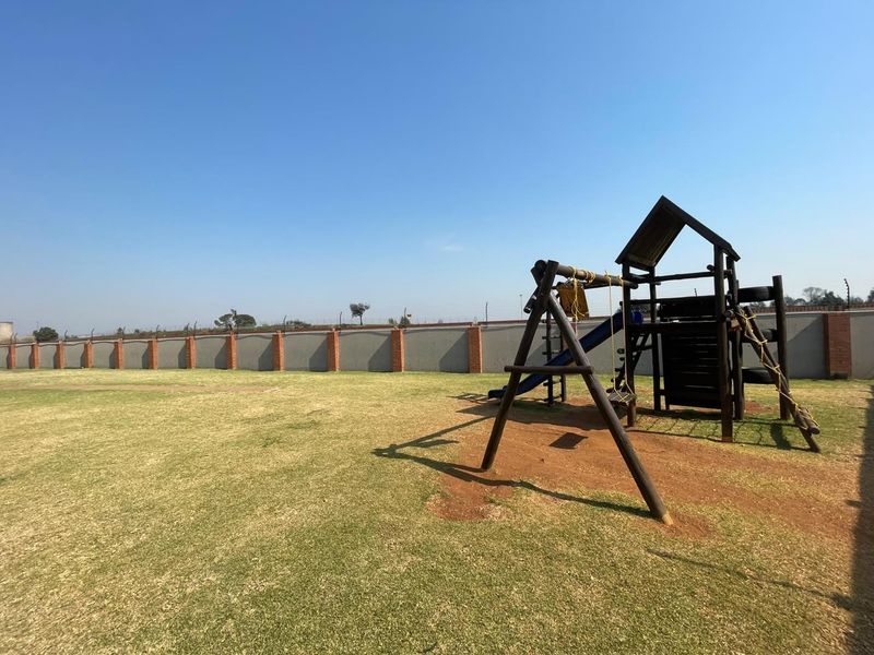 A spacious communal garden area featuring a large lawn and perimeter wall with electric fencing, suitable for outdoor recreation.