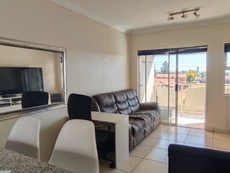 Open plan living area featuring tiled flooring, granite breakfast bar, and sliding glass doors leading to a balcony with natural light.