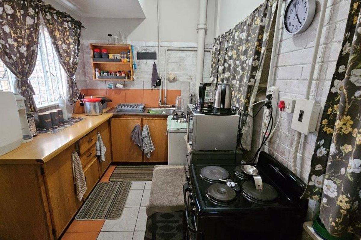 A compact, dated kitchen featuring wooden cabinetry, tiled splashbacks, and a freestanding electric stove, offering a functional layout with potential for modernization.