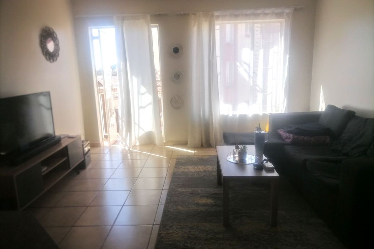 A bright living room featuring tiled flooring and large windows with access to an adjoining balcony, providing natural light throughout the space.