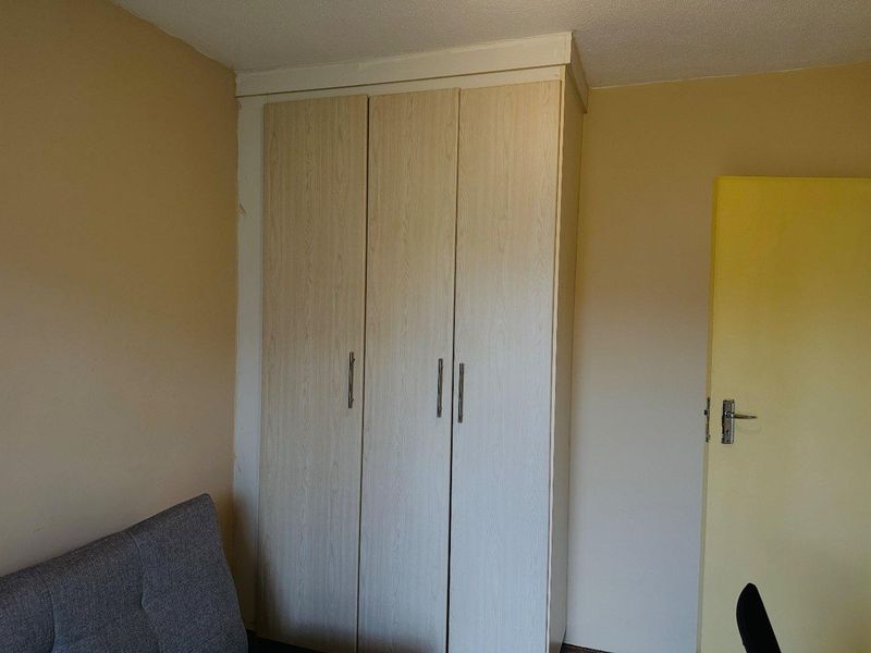 A bedroom featuring a light wood-finish built-in wardrobe and a standard internal door, showing signs of wear on the surrounding wall surfaces.