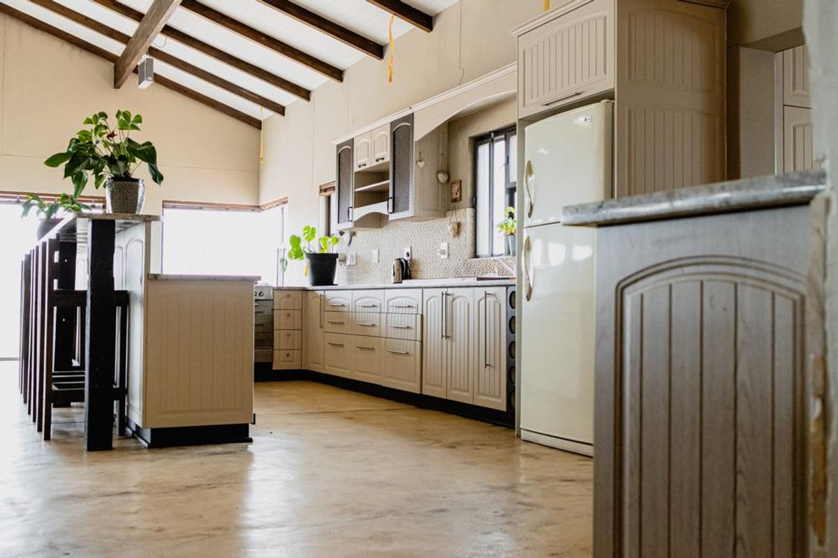 Spacious kitchen featuring exposed timber beams, ample built-in cabinetry, stone countertops, and a breakfast bar, offering a rustic yet functional culinary space.