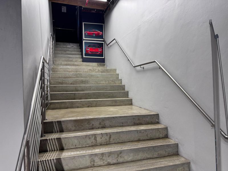 A functional concrete staircase featuring stainless steel handrails and an industrial-style exposed ceiling, providing access between levels.