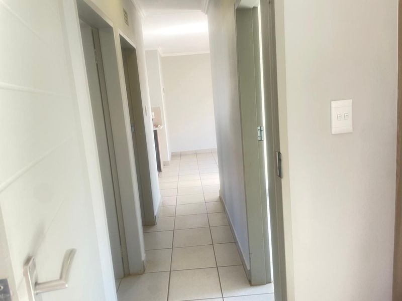 A clean, neutral hallway featuring tiled flooring and multiple internal door access points, connecting various rooms within the property.