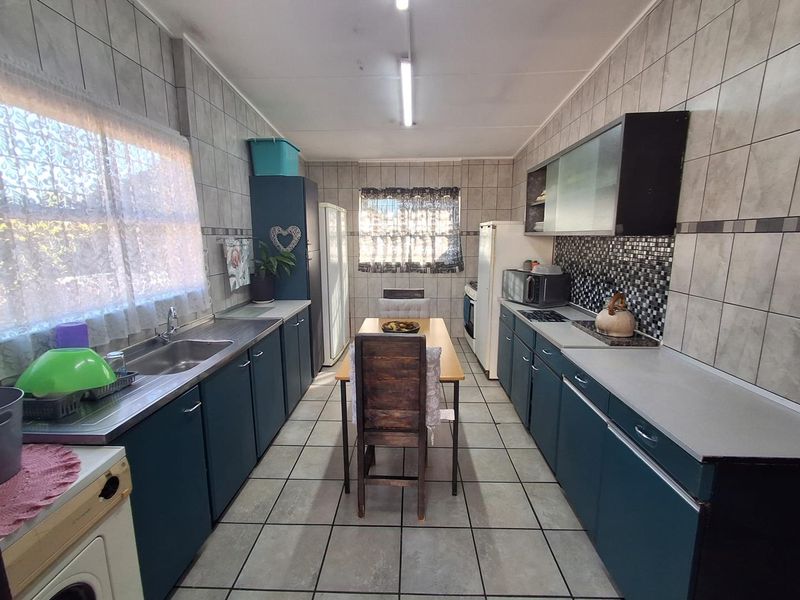 A functional kitchen featuring tiled walls and floors, ample built-in cabinetry, a stainless steel sink, and integrated cooking appliances.