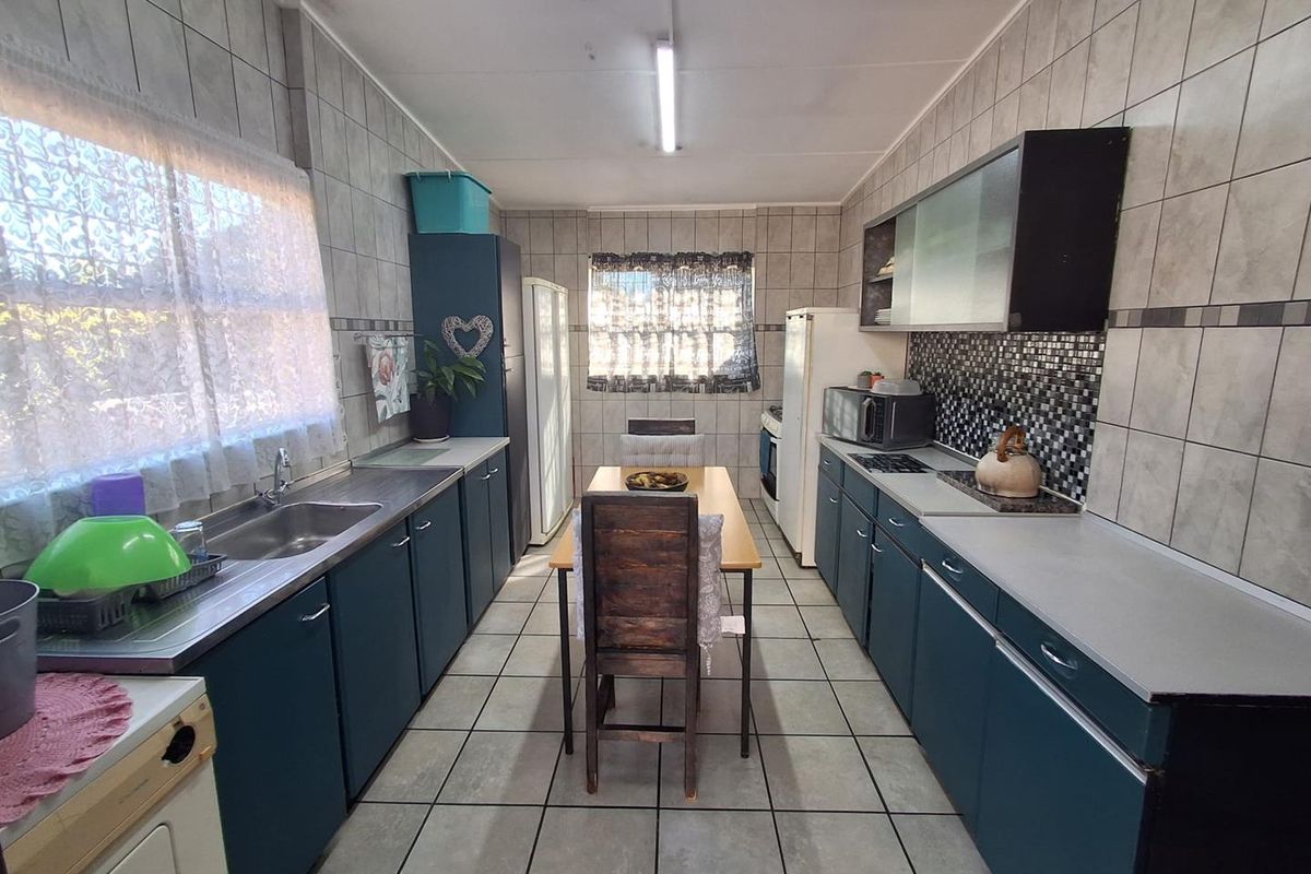 A functional kitchen featuring tiled walls and floors, ample built-in cabinetry, a stainless steel sink, and integrated cooking appliances.