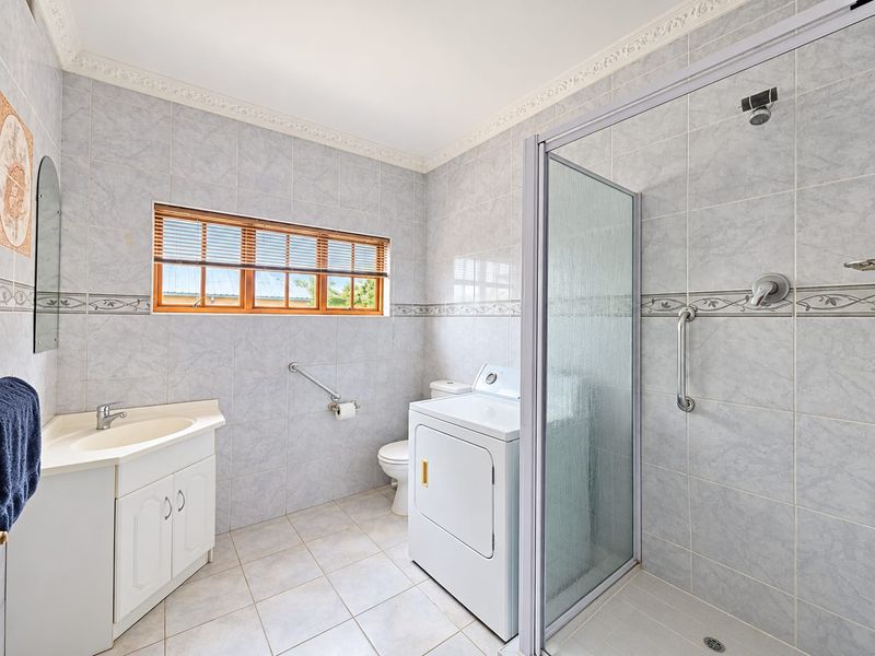 A functional bathroom featuring a shower enclosure, vanity with basin, toilet, and tiled finishes, with integrated laundry space.
