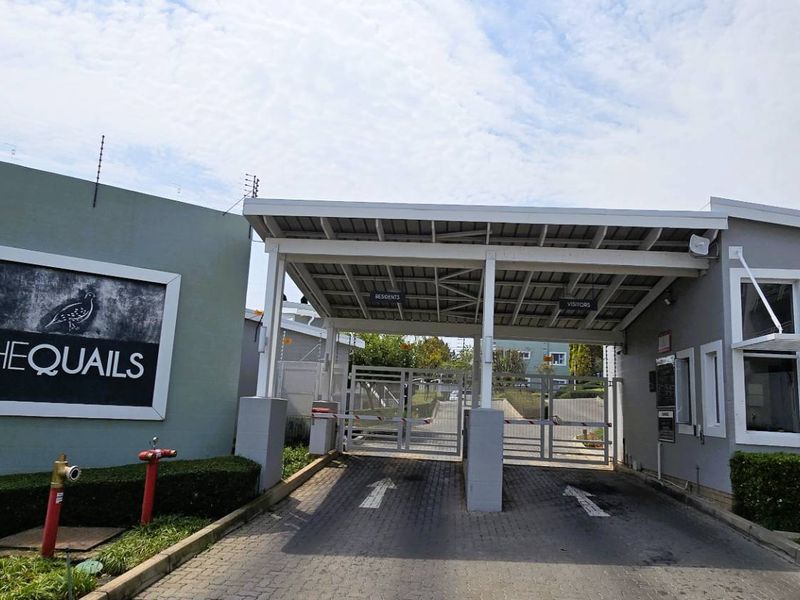 The secure entrance to The Quails apartment complex, featuring a gated access point, boom gate, and perimeter electric fencing.