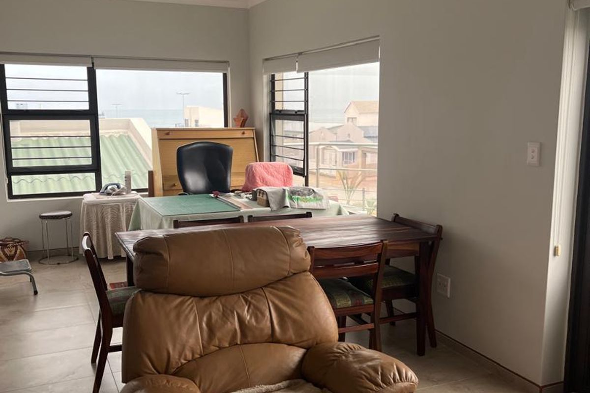 A bright living area featuring large windows with natural light, tiled flooring, and neutral wall finishes, offering a versatile space for relaxation or work.