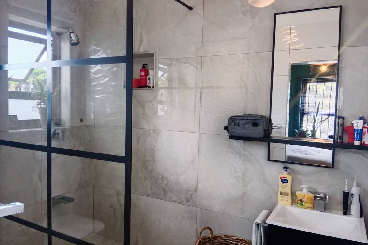 Modern bathroom featuring a walk-in shower with a black-framed glass screen, large-format wall tiles, and a sleek wall-mounted vanity unit.