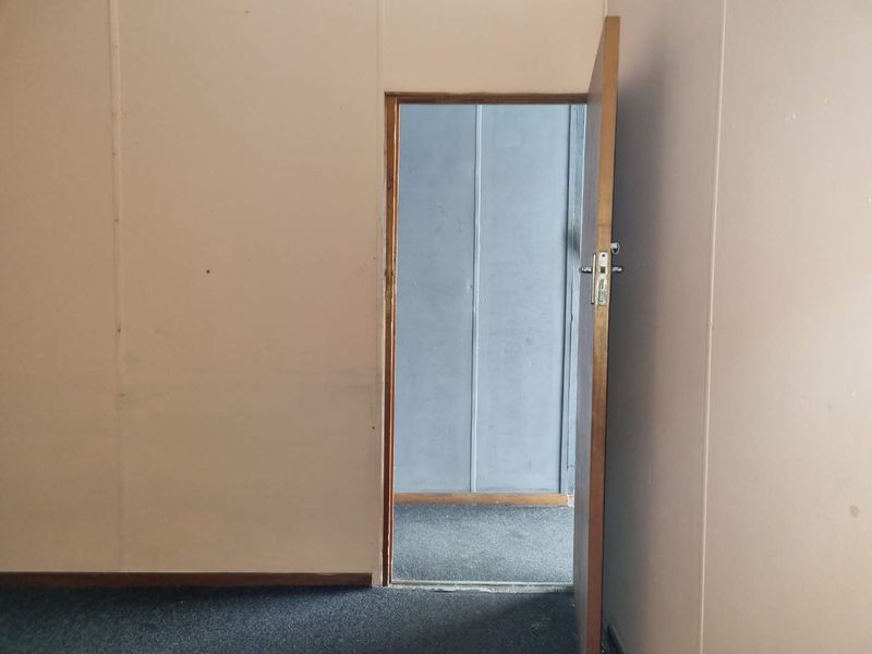 An empty interior space featuring panelled walls, carpet flooring, and a timber door leading to an adjacent room.