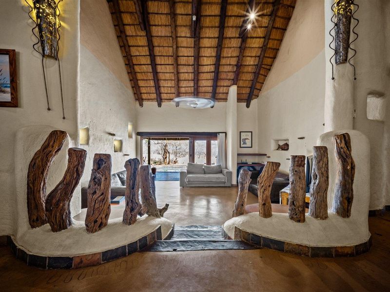 Spacious living area featuring a high vaulted thatched ceiling, exposed timber beams, textured plaster walls, and seamless access to the outdoor patio.