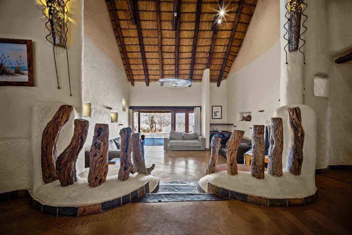 Spacious living area featuring a high vaulted thatched ceiling, exposed timber beams, textured plaster walls, and seamless access to the outdoor patio.