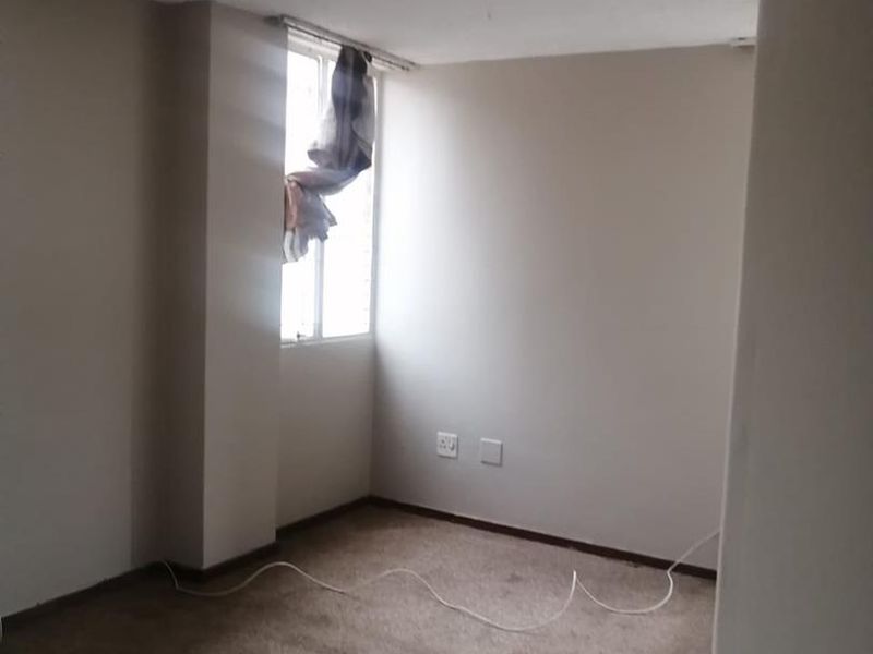 An empty bedroom featuring neutral walls, carpet flooring, and a single window, providing a blank canvas for potential interior design updates.