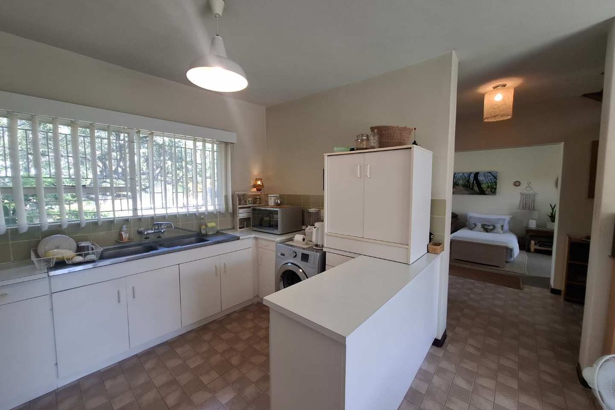 A functional kitchen featuring white cabinetry, a double basin sink, and a breakfast bar, with an adjacent view into the bedroom area.