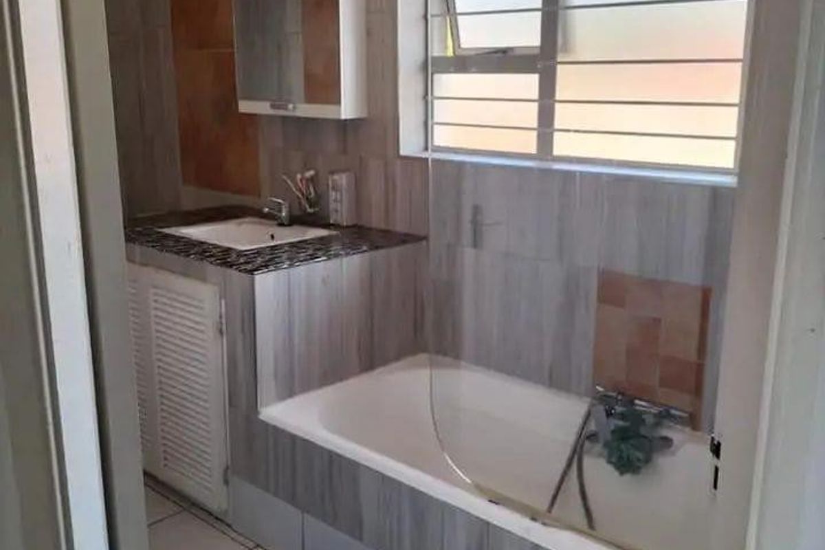 A functional bathroom featuring a built-in vanity, bathtub, and tiled finishes, offering a practical layout with natural light from the window.