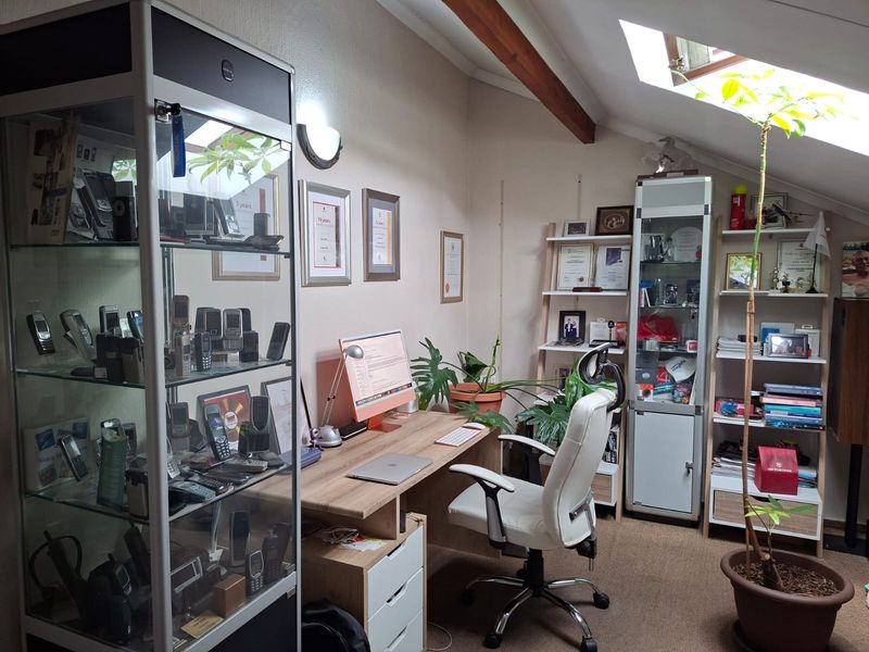 A well-lit home office featuring a sloped ceiling with a skylight, exposed timber beams, and built-in desk cabinetry.