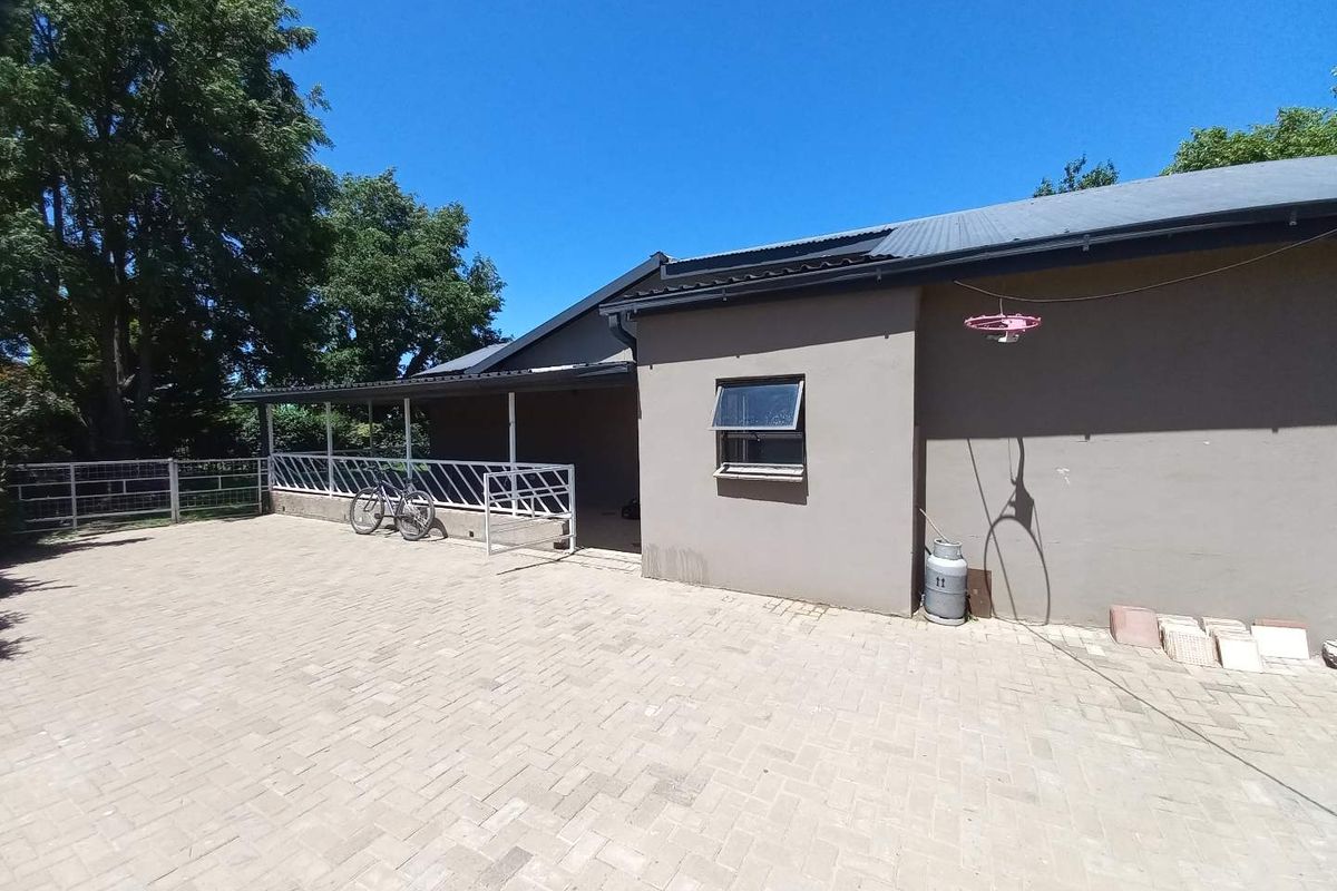 A spacious paved rear courtyard area featuring a covered patio section, metal security railing, and a neutral rendered exterior wall finish.