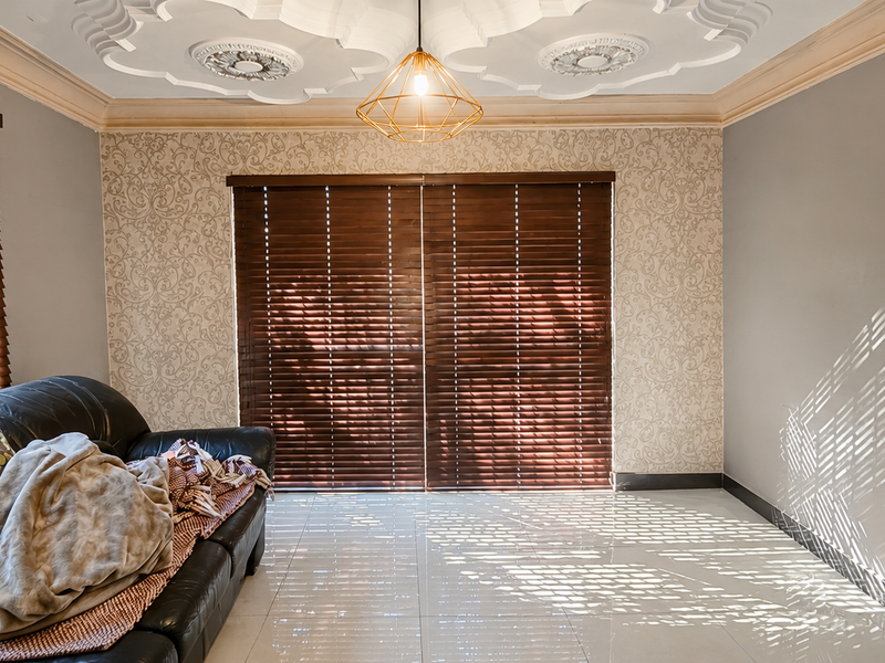 A living room featuring decorative crown molding, an ornate ceiling rose, tiled flooring, and wooden venetian blinds providing natural light control.