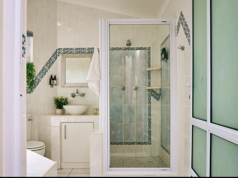 A functional bathroom featuring a glass-enclosed shower, built-in vanity with a vessel sink, and decorative tiled wall accents.