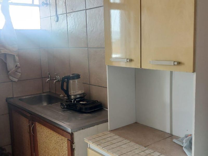 A functional scullery area featuring built-in cabinetry, a stainless steel sink, and tiled wall finishes, offering potential for modernization.
