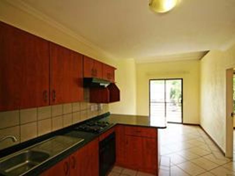 A functional kitchen featuring wood-finish cabinetry, dark countertops, built-in appliances, and tiled flooring, leading to an adjacent living area with sliding door access.