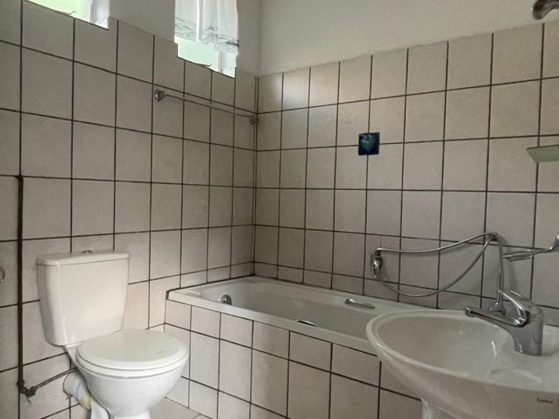 A functional bathroom featuring a pedestal basin, built-in bathtub, and toilet with tiled finishes throughout, offering potential for modernization.