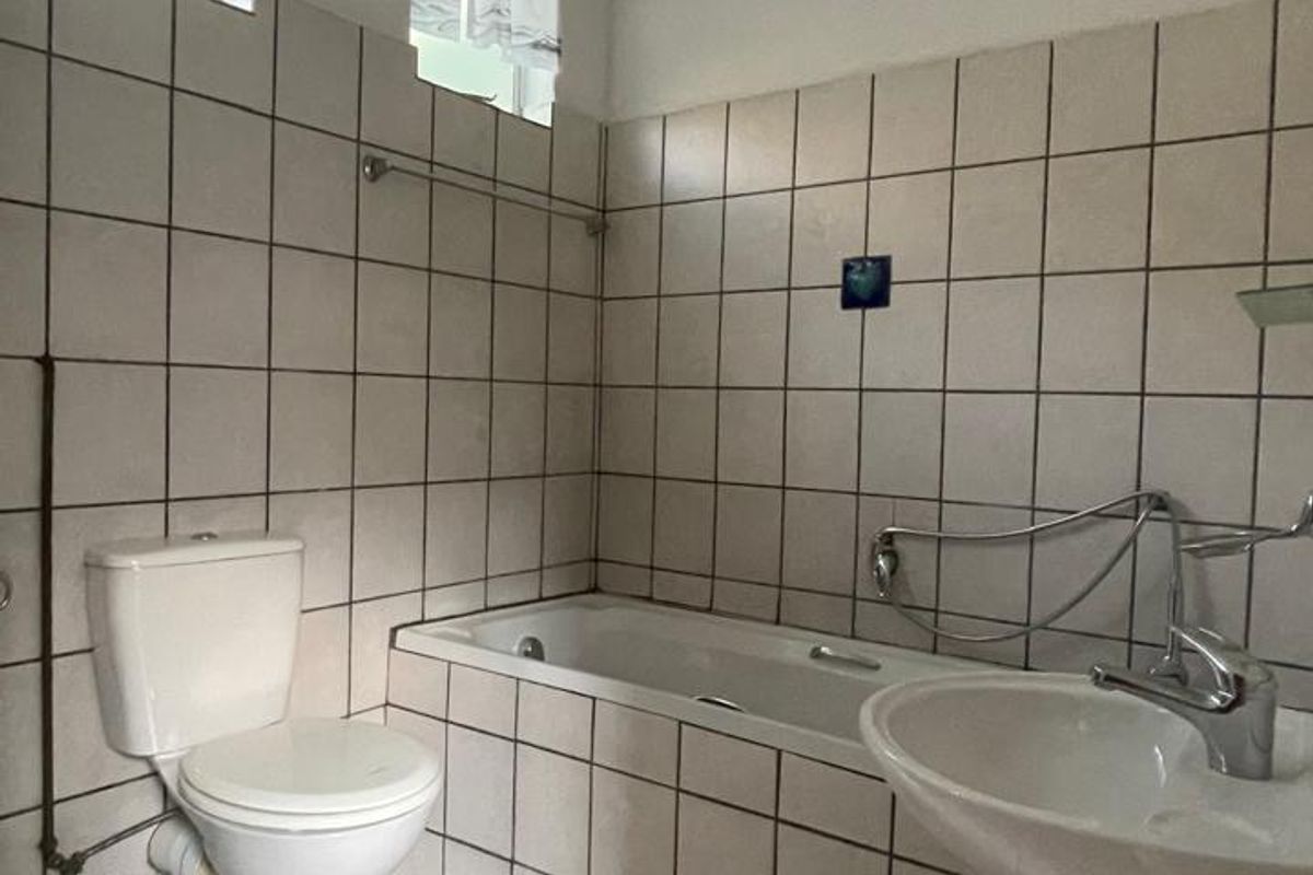 A functional bathroom featuring a pedestal basin, built-in bathtub, and toilet with tiled finishes throughout, offering potential for modernization.