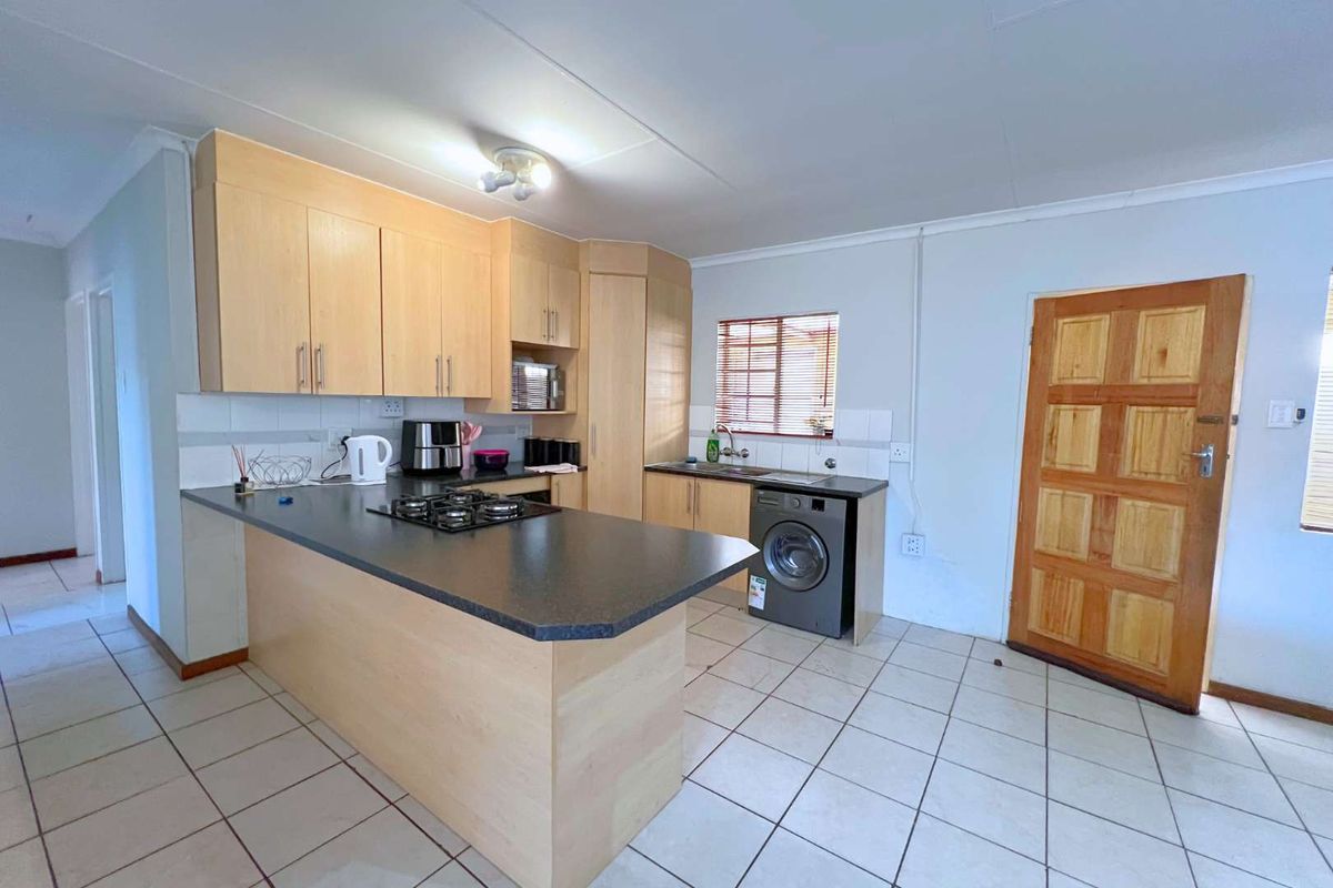 Functional kitchen featuring light wood cabinetry, dark laminate countertops, a built-in gas hob, and tiled flooring with direct access to an exterior door.