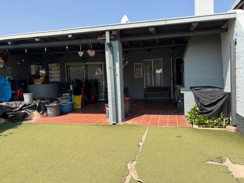 A covered outdoor patio area featuring tiled flooring and a built-in fireplace, overlooking a backyard with artificial lawn.