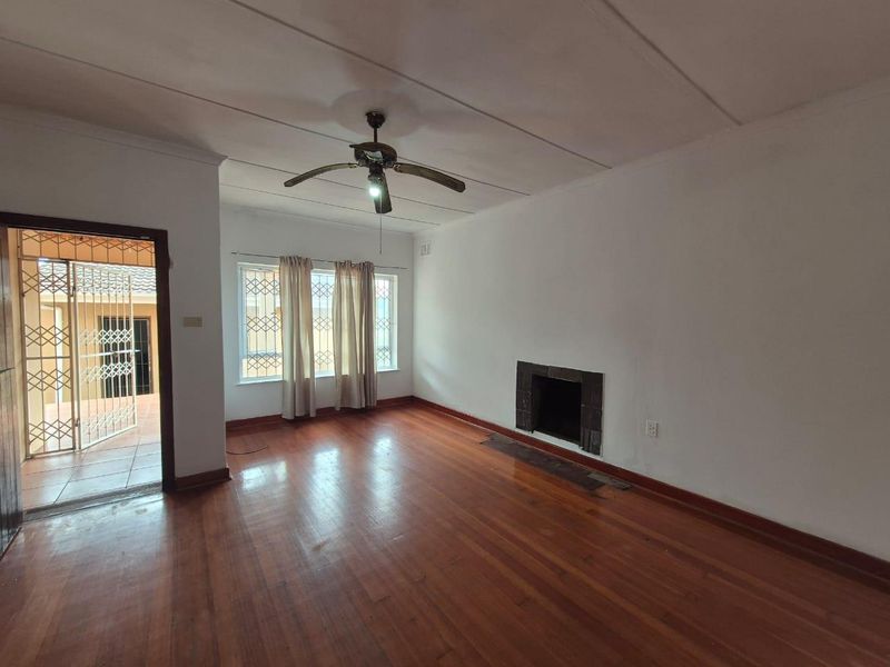 Spacious living room featuring original hardwood flooring, a built-in fireplace, and a ceiling fan, with direct access to an outdoor patio area.
