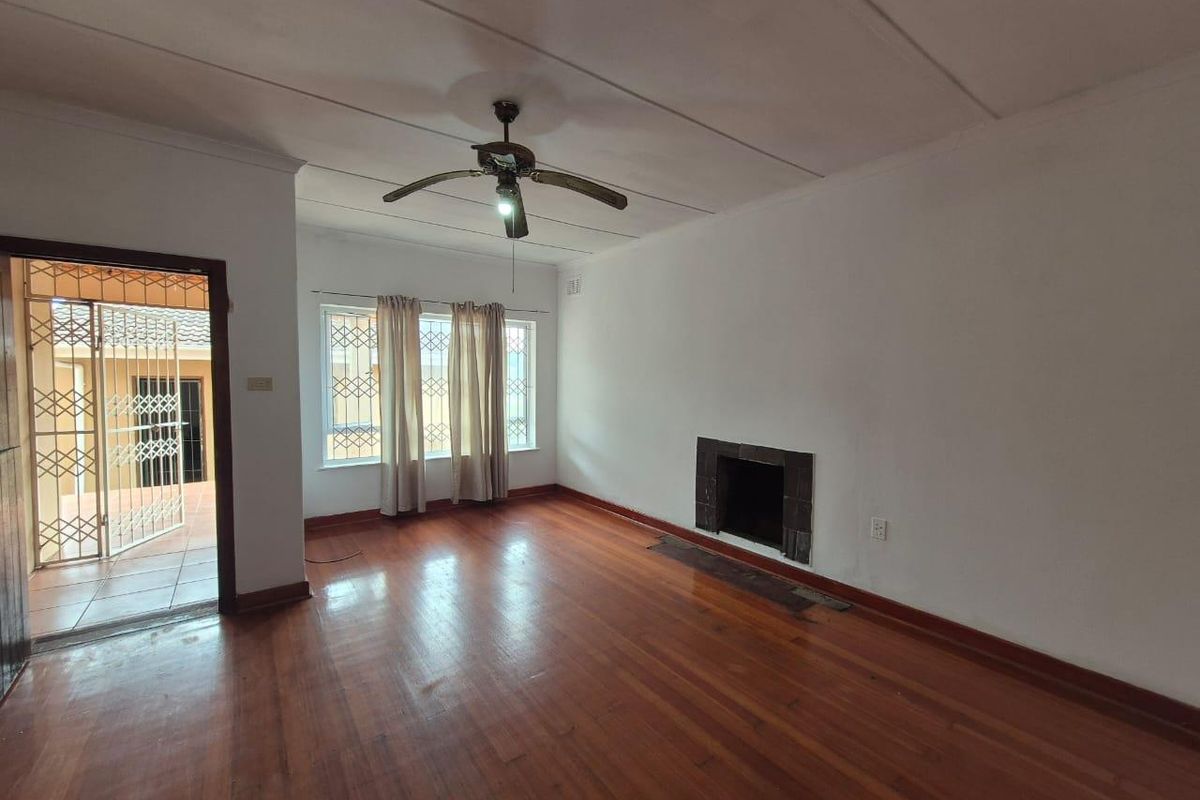 Spacious living room featuring original hardwood flooring, a built-in fireplace, and a ceiling fan, with direct access to an outdoor patio area.