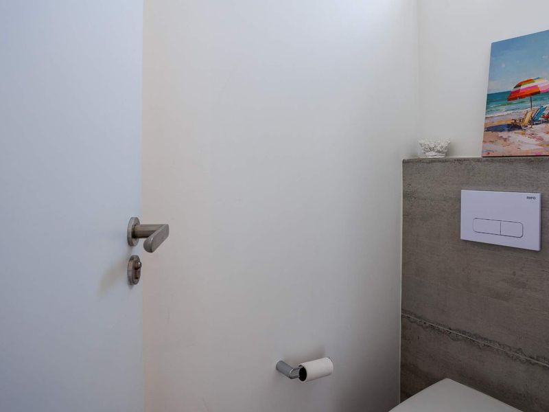 A modern bathroom featuring a minimalist wall-mounted toilet flush plate and a contemporary exposed concrete feature wall.